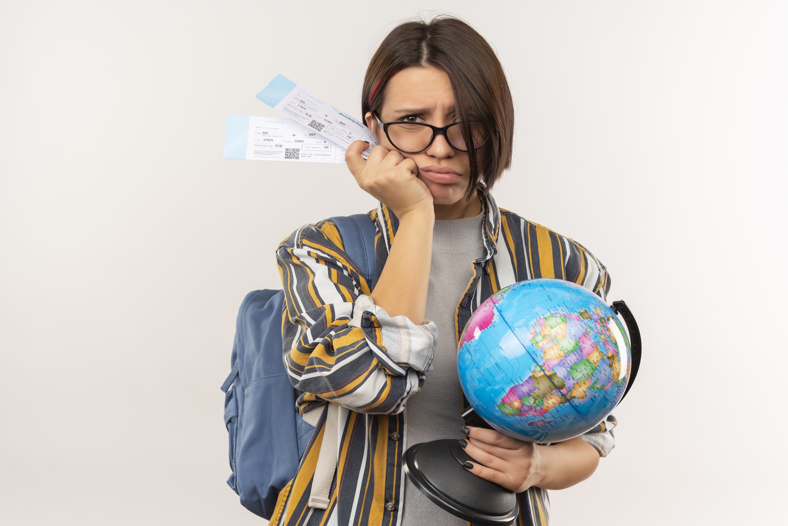 unpleased young student girl wearing glasses and back bag holding airplane tickets and globe isolated on white background with copy space